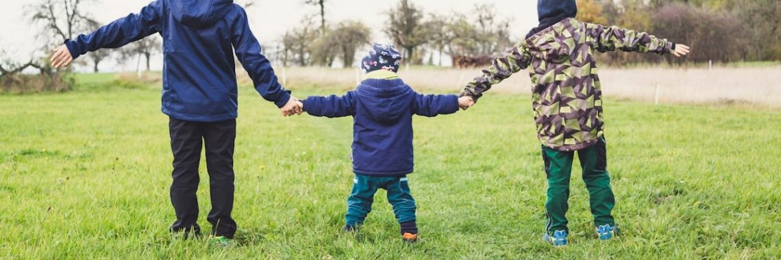 three children holding hands standing on grasses